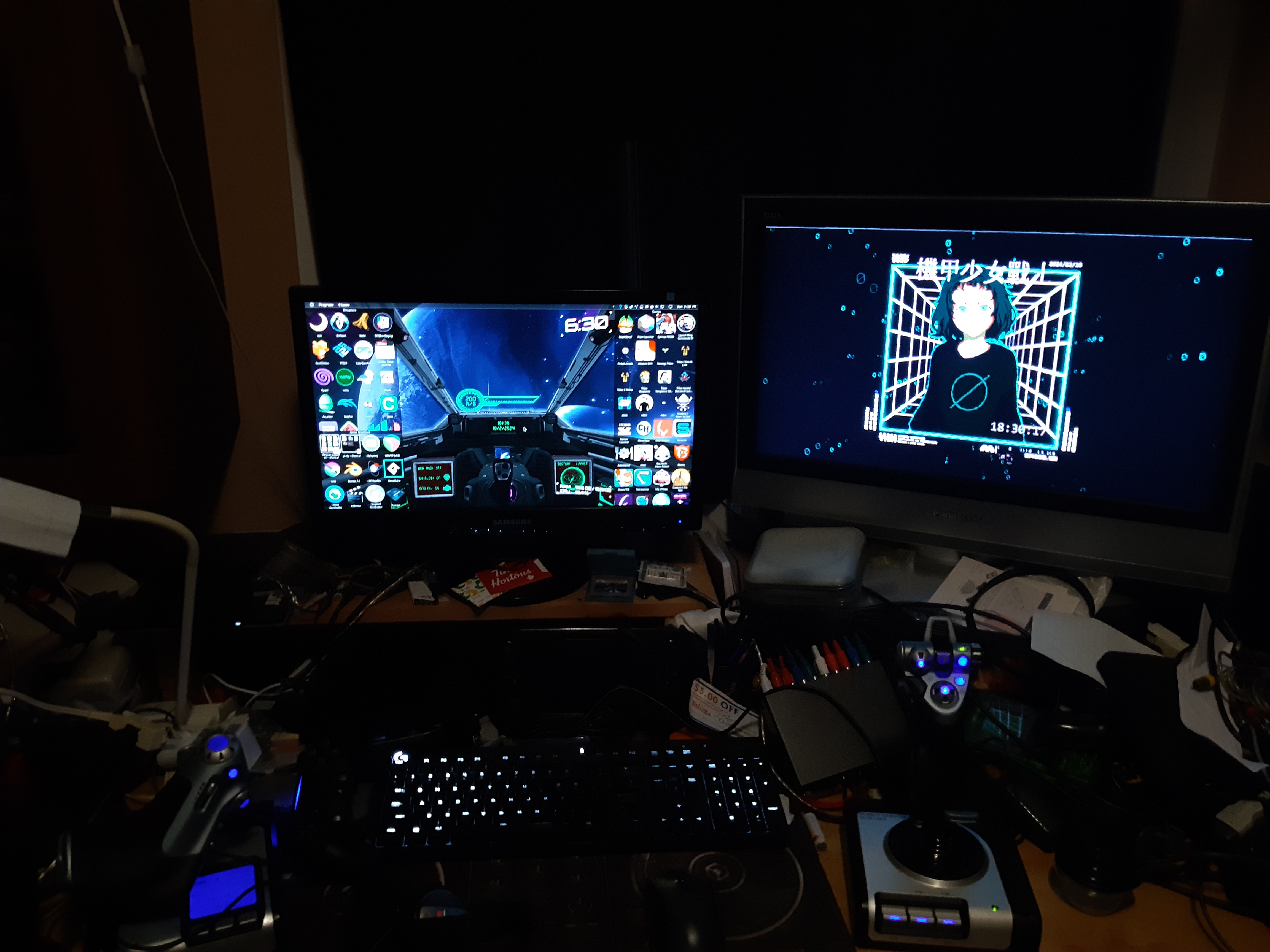 real-life picture of the same desktops, showing the backlit keyboard, the obscene mess on the desk and a HOTAS flightstick